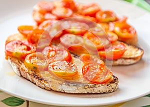 Grilled sliced fresh cherry tomatoes on buttered toasted sough dough bread on a white plate.