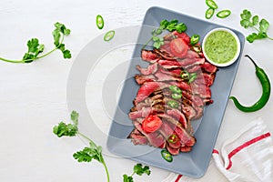 Grilled and sliced rare beef skirt steak served with green chimichurri sauce photo