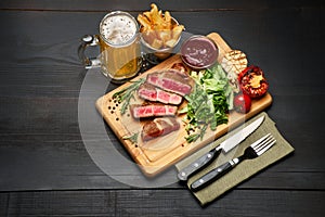 Grilled sliced roated beef steaks, potato and sauce on wooden cutting board photo