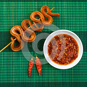 Grilled snake on skewer with chili sauce and rice on white plate on mat