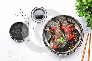 Grilled spicy eggplant with hot red chili peppers, soy sauce, garlic and sesame seeds in asian style, white table background, top