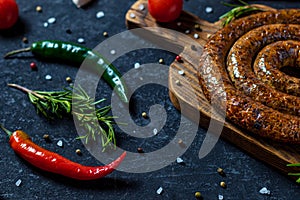 Grilled spiral sausages with garlic and seasoning on dark wooden background