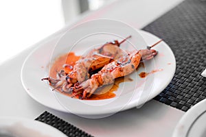 Grilled Squids on wooden sticks on white plate in spicy sause. A dish of Chinese cuisine.