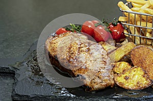 Grilled steak with baked potatoes and roast tomato. Top view Pork chop serve with gilled potato on black slate board.  Home made