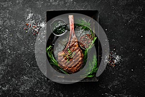 Grilled steak on the bone. Tomahawk steak on a black stone background. Top view. Free copy space