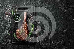 Grilled steak on the bone. Tomahawk steak on a black stone background. Top view. Free copy space