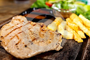 Grilled steak with french fries and vegetables served on wooden board