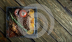 Grilled steak with knife and fork carved on black stone slate. Steak on a hot marble stone. Copy space, dark background