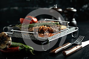 Grilled steak with knife and fork carved on black stone slate. Steak on a hot marble stone. Copy space, dark background