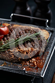 Grilled steak with knife and fork carved on black stone slate. Steak on a hot marble stone. Copy space, dark background