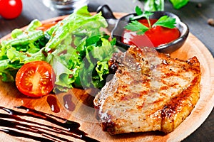 Grilled steak pork with fresh vegetable salad, tomatoes and sauce on wooden cutting board