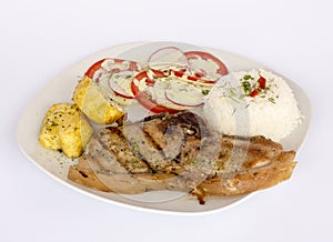 Grilled steak pork meat with salad, rice, potatoes, tomatoes served with a glass of chicha.