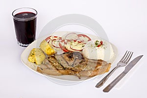 Grilled steak pork meat with salad, rice, potatoes, tomatoes served with a glass of chicha.