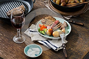 Grilled steak with potatoes, salad on wooden table with wine