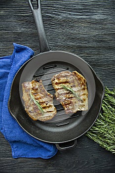 Grilled steak on a round grill pan, garnished with spices for meat, rosemary, greens and vegetables on a dark wooden background