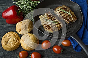 Grilled steak on a round grill pan, garnished with spices for meat, rosemary, greens and vegetables on a dark wooden background