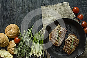 Grilled steak on a round grill pan, garnished with spices for meat, rosemary, greens and vegetables on a dark wooden background