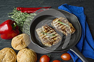 Grilled steak on a round grill pan, garnished with spices for meat, rosemary, greens and vegetables on a dark wooden background