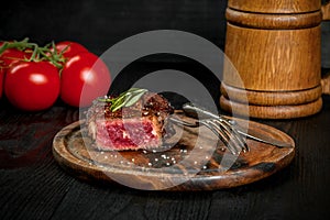 Grilled steak seasoned with spices and fresh herbs served on a wooden board with wooden mug of beer and fresh tomato