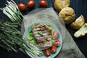 Grilled steak served on a plate, decorated with spices for meat, rosemary, greens and vegetables on a dark wooden background