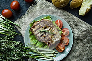 Grilled steak served on a plate, decorated with spices for meat, rosemary, greens and vegetables on a dark wooden background