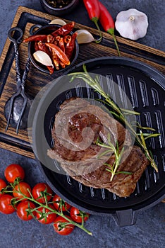 Grilled striploin beef steak on grill pan with tomato, herbs and