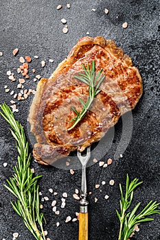 Grilled Striploin steak or strip new York on a meat fork. Black background. Top view