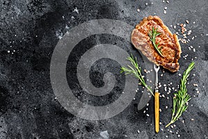 Grilled Striploin steak or strip new York on a meat fork. Black background. Top view. Copy space