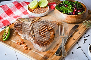 Grilled t-bone or porterhouse steak seasoned with rosemary in a rustic kitchen on a wooden board with salad