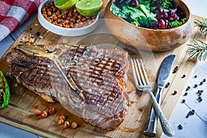 Grilled t-bone or porterhouse steak seasoned with rosemary in a rustic kitchen on a wooden board with salad