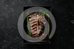 Grilled T-bone steak with spices in a metal baking dish on a black background. Top view. Rustic style