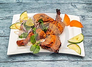 Grilled tandoori chicken with lemon and onion served in dish isolated on wooden table top view of indian spicy food