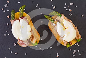 Grilled toast with asparagus in bacon and poached egg on wooden background