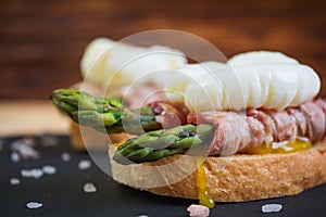 Grilled toast with asparagus in bacon and poached egg on wooden background