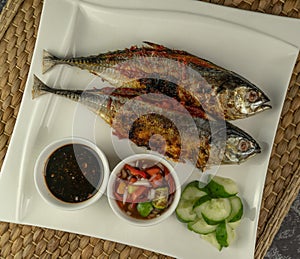 Grilled Torpedo Scad fish Ikan Cencaru Bakar in Malay with hot soy sauce, hot tamarind juice and fresh cucumber on white plate photo