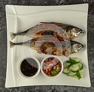 Grilled Torpedo Scad fish Ikan Cencaru Bakar in Malay with hot soy sauce, hot tamarind juice and fresh cucumber on white plate