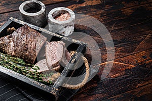 Grilled Tri Tip steak, sirloin bottom beef in a tray with herbs. Wooden background. Top view. Copy space