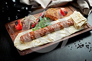 Grilled Turkish adana kebab with grilled vegetables, onion and rice on a wooden board. Dark background