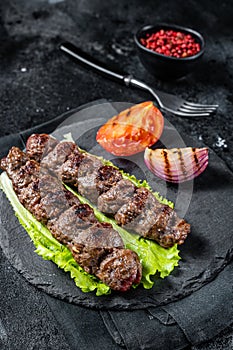 Grilled Urfa kebab with tomato, salad and onion. Black background. Top view