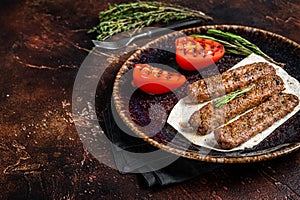 Grilled Urfa shish kebab on a plate with tomato. Dark background. top view. Copy space