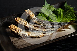 Grilled urume sardines on a black table. A side dish of sake