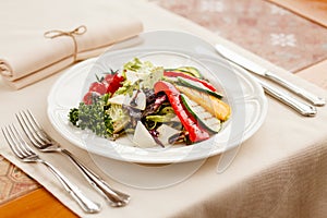 Grilled vegetables with cheese and herbs, seasoned with balsamic vinegar. served on a white round plate on a style covered with a