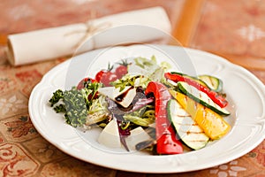 Grilled vegetables with cheese and herbs, seasoned with balsamic vinegar. served on a white round plate on a wooden table top