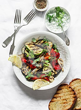 Grilled vegetables eggplant, zucchini, pepper salad with tzadziki Greek yogurt sauce on a light background, top view. Delicious