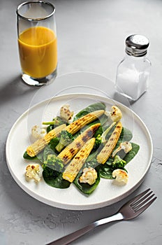 Grilled vegetables and juice on a light stone background, dietary vegetarian snack babycorn, healthy low-calorie food, vertical