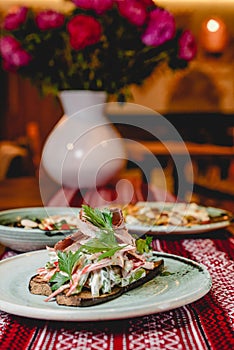 Grilled vegetables and meat served in a ceramic plate on a rustic wooden table with traditional tablecloth.