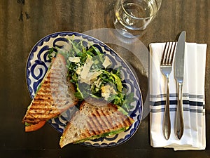 Grilled vegetarian sandwich with arugula-parmesan salad on table