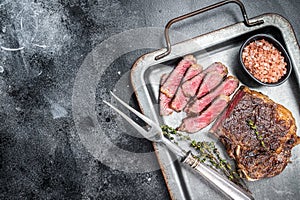 Grilled Wagyu Striploin beef meat steak or new york steak in a steel tray. Black background. Top view. Copy space