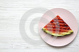 Grilled watermelon on a pink plate over white wooden background, from above. Healthy summer fruit.