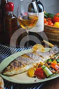 Grilled white fish on a dish on a table in a restaurant with a glass of white wine.